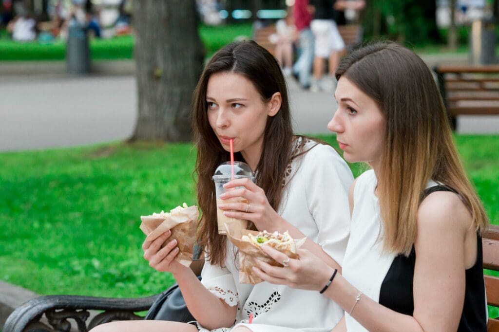 Caucasian women eats hamburger fast food sandwich on the street outdoors. Active girls hungry and