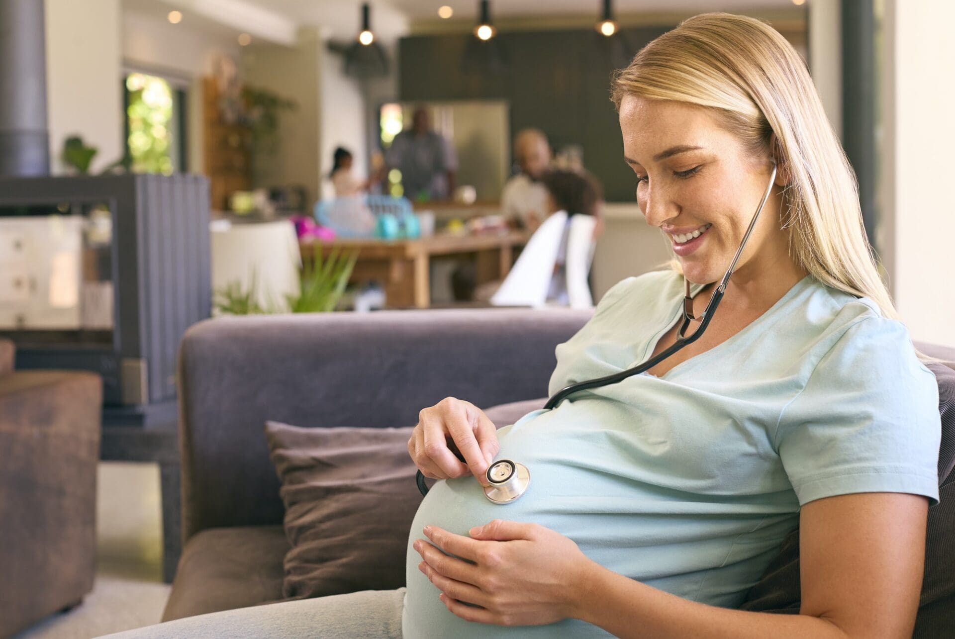 Pregnant Woman At Home Listening To Baby Heartbeat With Stethoscope
