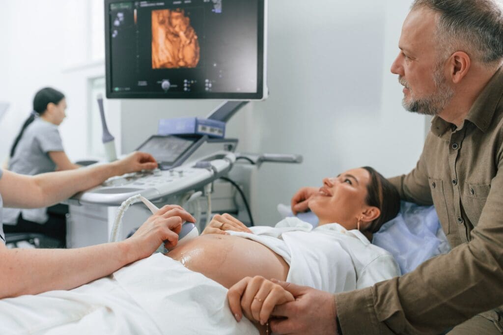 supporting his wife. Pregnant woman is lying down in the hospital, doctor does ultrasound